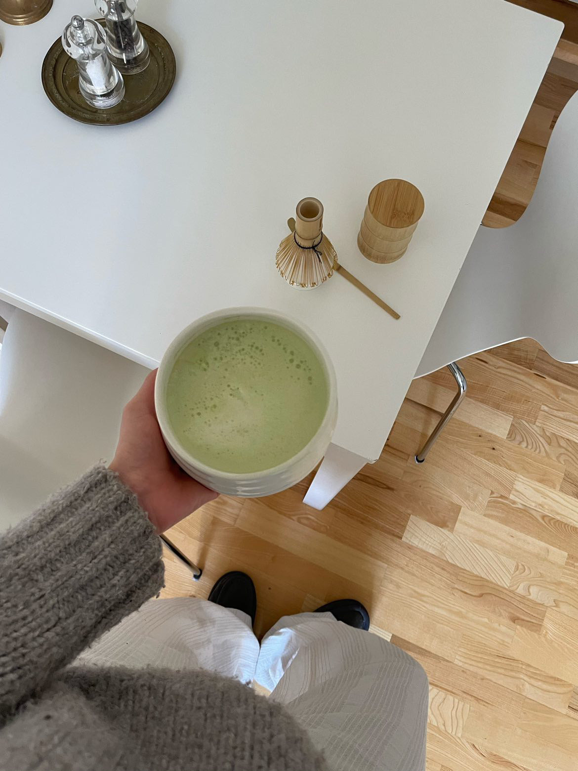 En kop Matcha Latte i en keramikkop med en bambuspisk, bambusske og bambusbeholder i baggrunden.